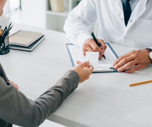 Person handing card to dentist across desk