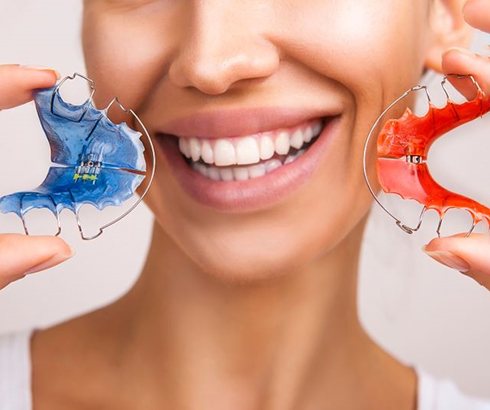 Woman holding two orthodontic retainers next to her smile?