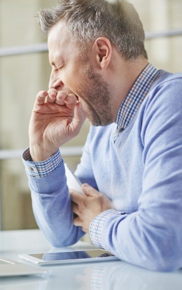 Older man covering mouth while yawning