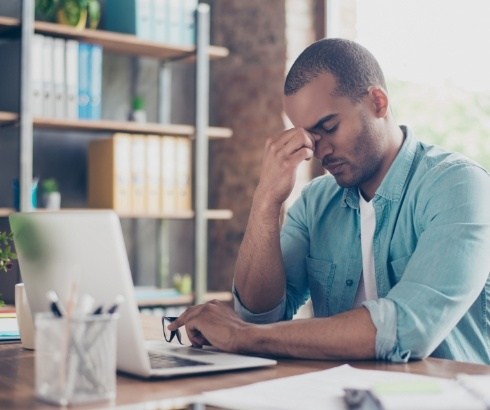 Man sitting desk and pinching bridge of nose in frustration