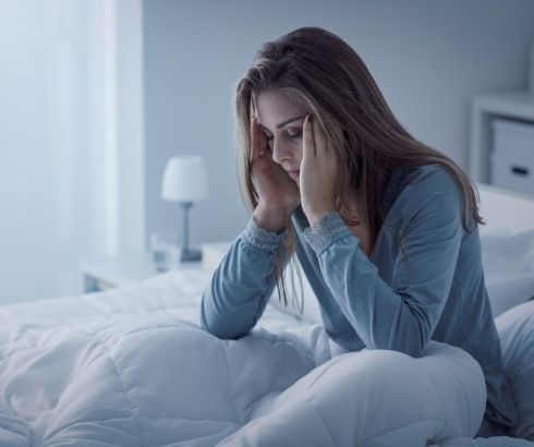 Woman touching her temples while sitting up in bed at night