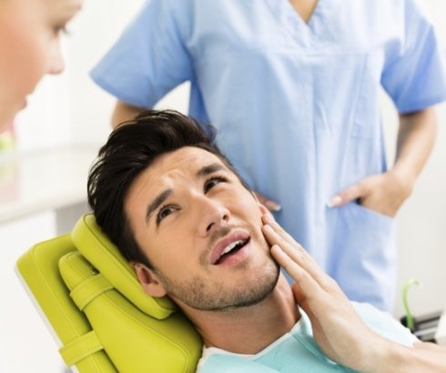 Man holding his jaw in pain while talking to dentist