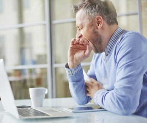 Yawning man sitting at desk with laptop