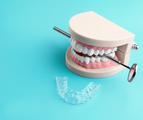 Model of teeth holding dental mirror next to clear aligner