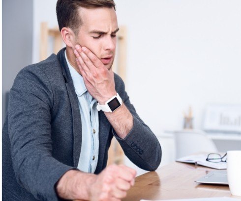 Man sitting at desk and holding side of his face in pain