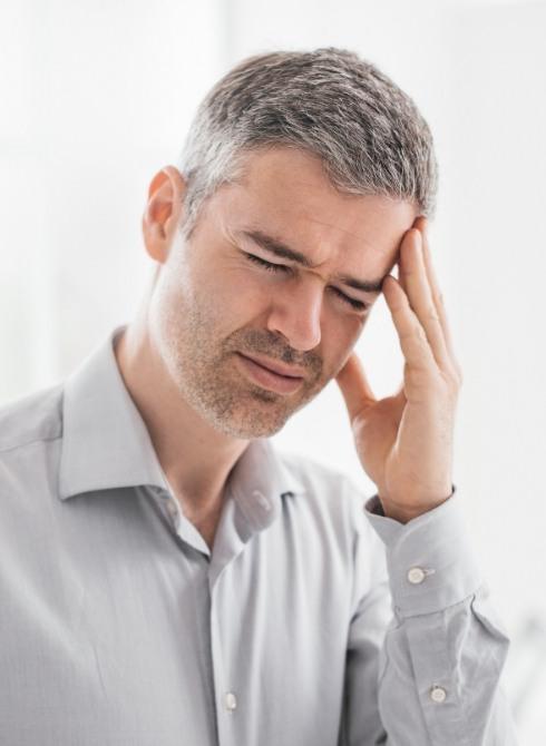 Man in white shirt holding his temple in pain