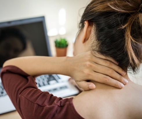 Woman sitting at computer holding back of her neck in pain