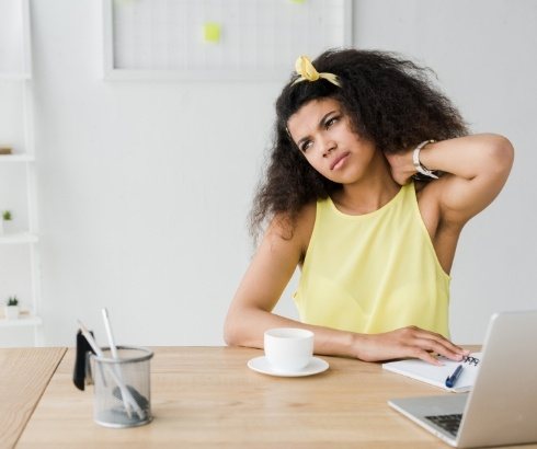 Woman sitting at desk with laptop holding back of her neck in pain