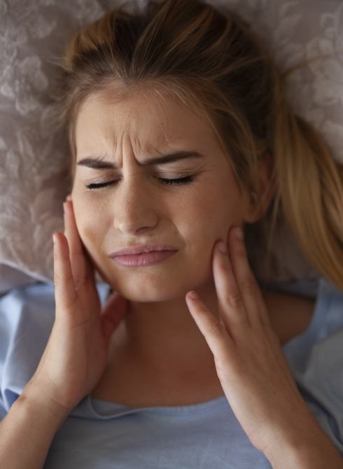 Woman laying in bed holding both cheeks in pain