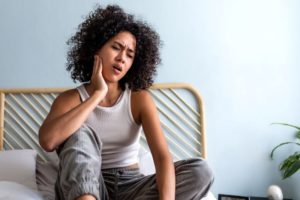 Woman sitting on bed, struggling with jaw pain