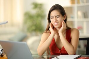 Woman sitting at her computer, suffering TMJ pain