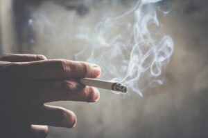 Hand holding smoldering cigarette.